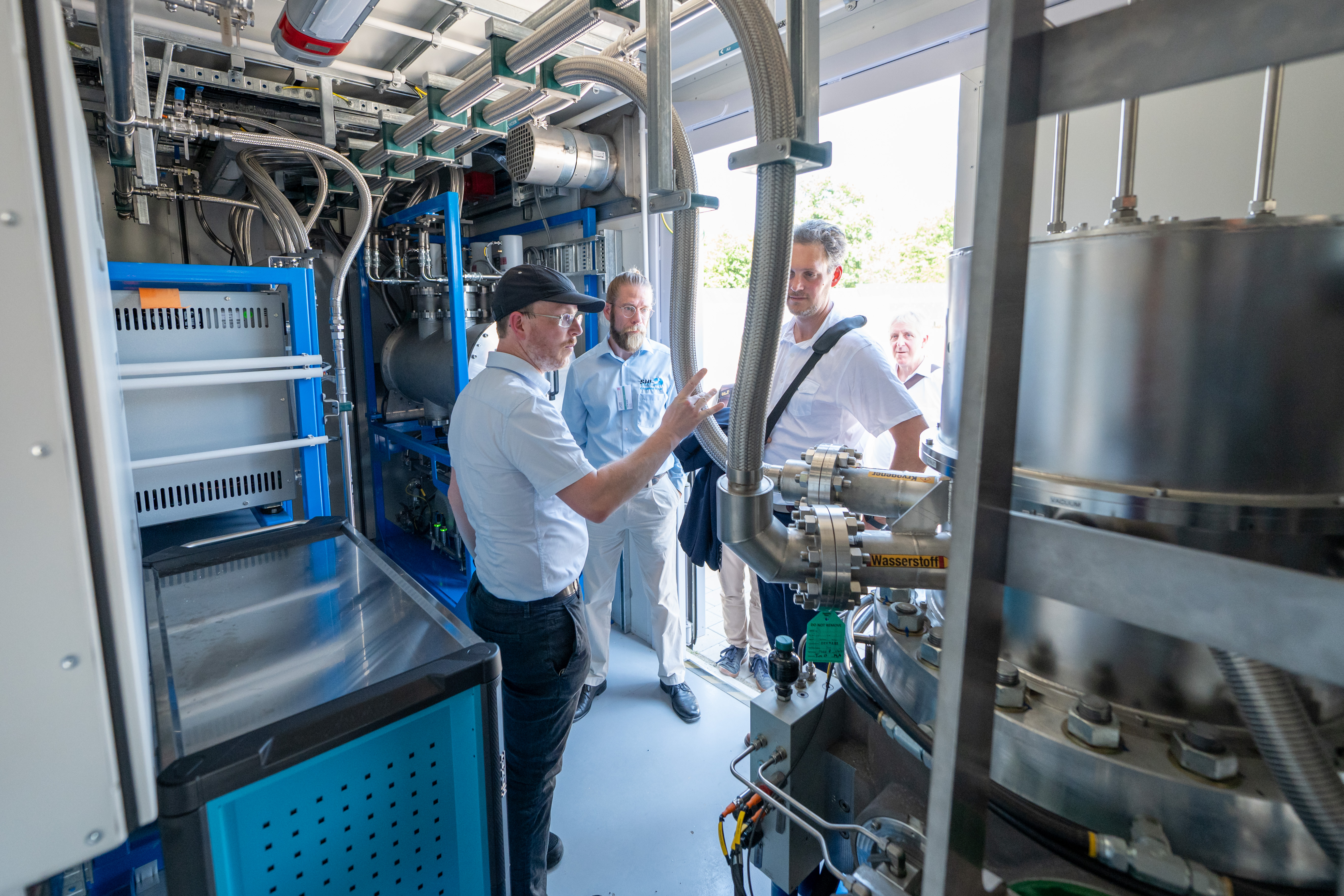 Experten besprechen eine industrielle Wasserstoffanlage in einem Technikraum.